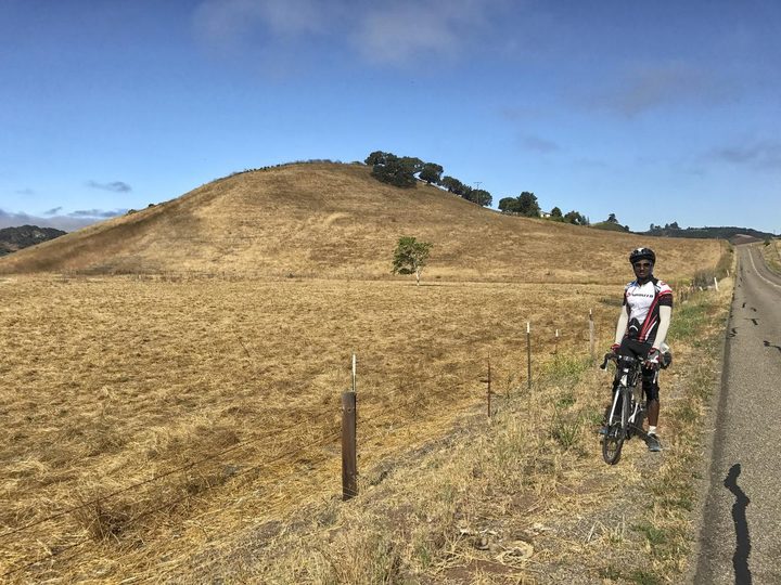 Standing with the bike on the shoulder of a country road beside dry golden hills